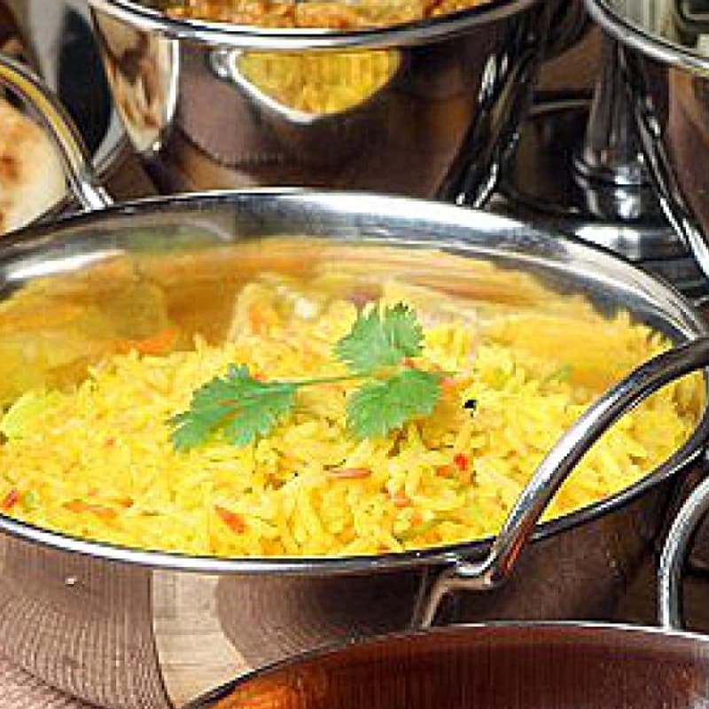 A spread of balti dishes in steel karahi with pilau rice and naan.