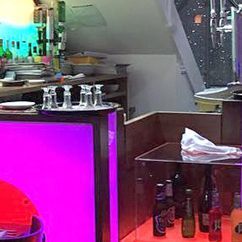 The bar area, lit in pink and purple, with bottles and glassware on the counter.
