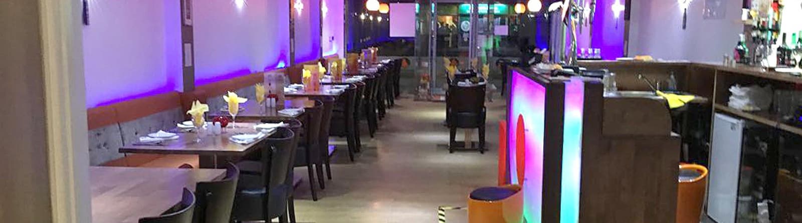 The dining room laid for service, banquette seating along the wall under violet lighting.